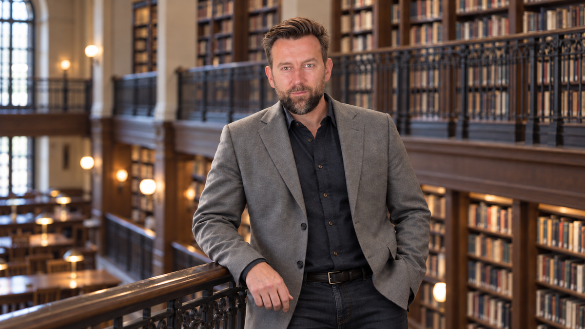 Sean Brownlee standing in a library lined with books